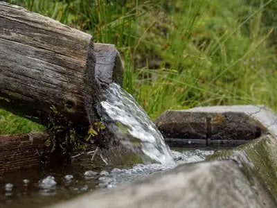 Witterer Holzscheittrichter, der klares Wasser in ein steinernes Becken gießt.